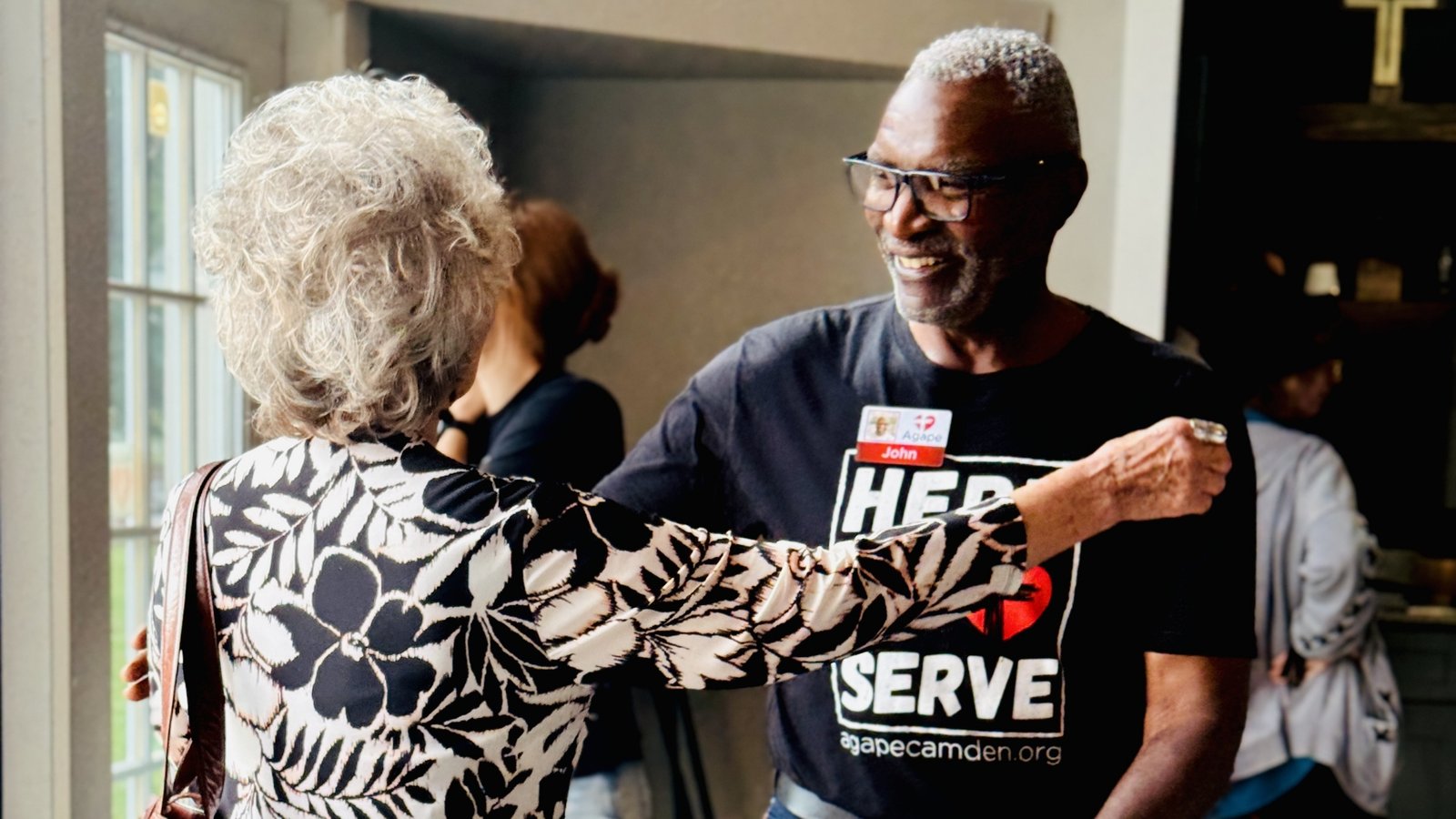 Volunteer in a Here to Serve shirt greeting a guest
