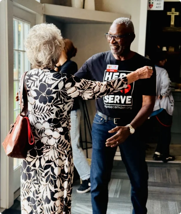 Volunteer in a Here to Serve shirt hugging a guest